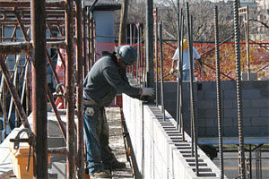 A worker pumps grout into the cores of concrete masonry units to embed the reinforcement and create strong walls.
