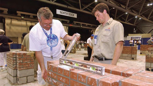 Nathan Rader (right) looks on as his instructor and father, David Rader, evaluates his completed composite project in the national masonry contest held in conjunction with the 45th Annual SkillsUSA National Leadership Conference in Kansas City, Mo. For his skill and effort, Rader earned second place honors in the secondary division.
