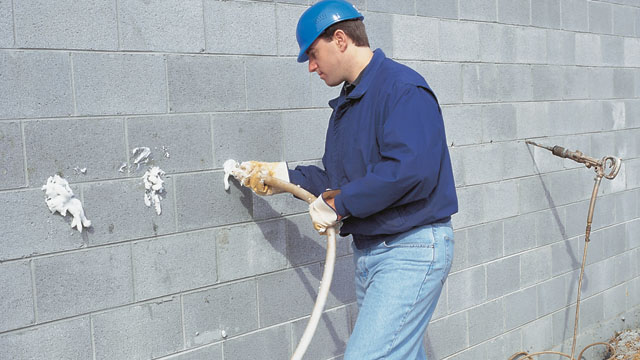 A wall is being filled with CMU foam using the side fill method by drilling 5/8-inch holes.