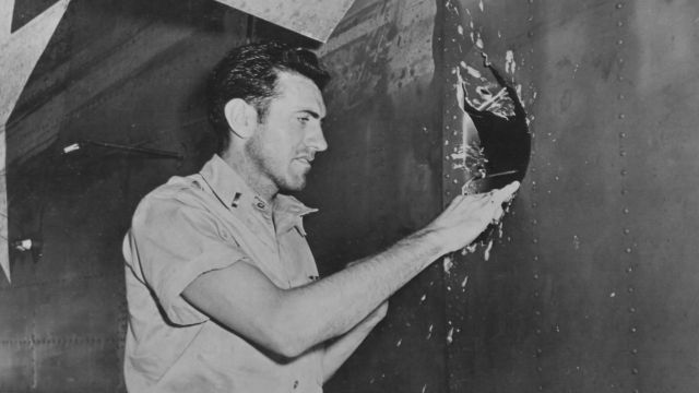 1Lt Louis Zamperini, bombardier of this B-24D Liberator 'Superman' peering through a hole in the aircraft from a 20mm shell over Nauru, Apr 20 1943; photo taken at Funafuti, Gilbert Islands; Source: United States National Archives